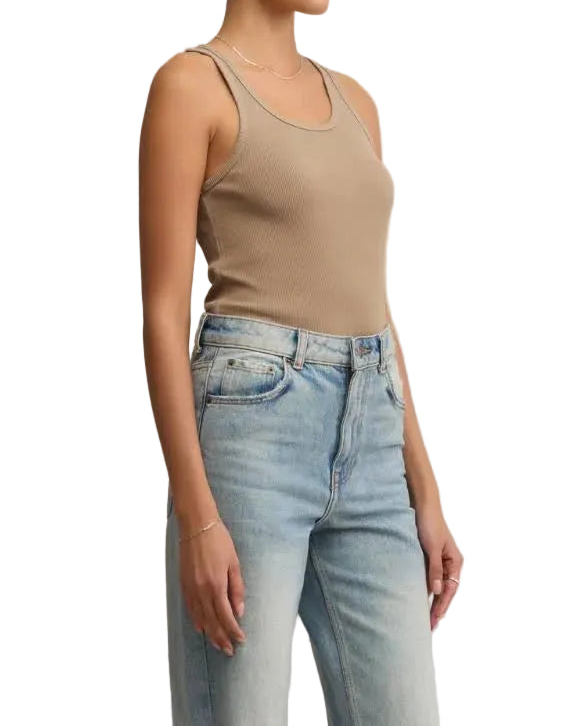 Woman wearing a beige tank top and light blue jeans against a beige background